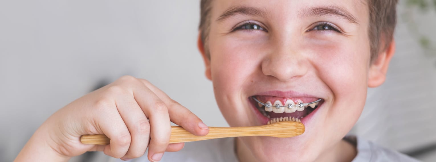 Ein Junge putzt sich die Zähne, an der eine feste Zahnspange befestigt ist. 