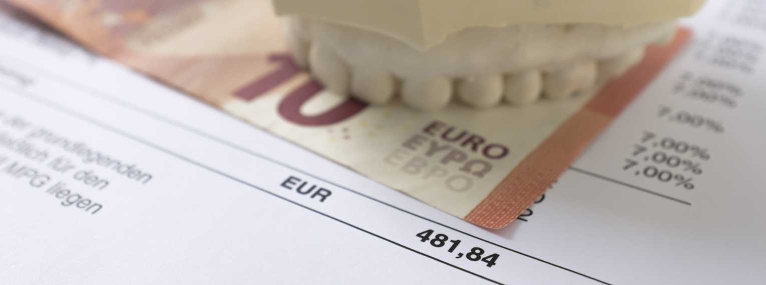 Ein 10 Euro Schein und ein Modell eines Gebisses liegen auf einer Zahnarztrechnung.