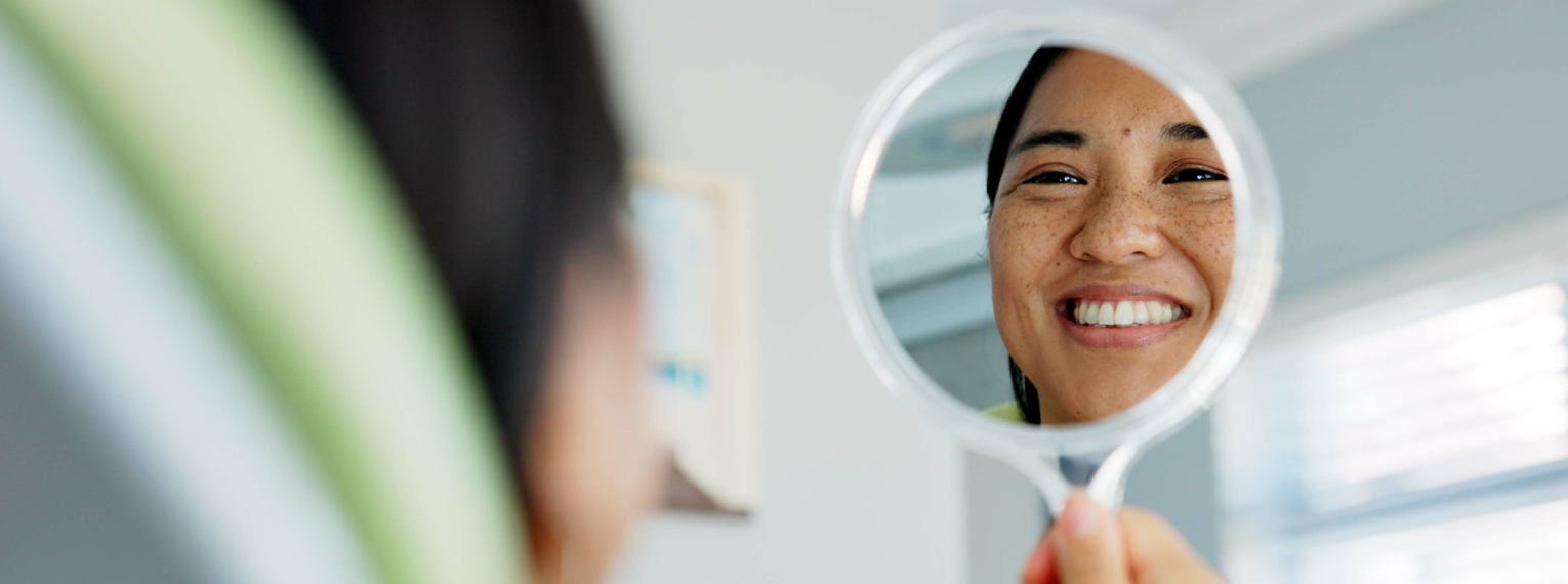 Eine Frau lächelt beim Zahnarzt in den Spiegel.