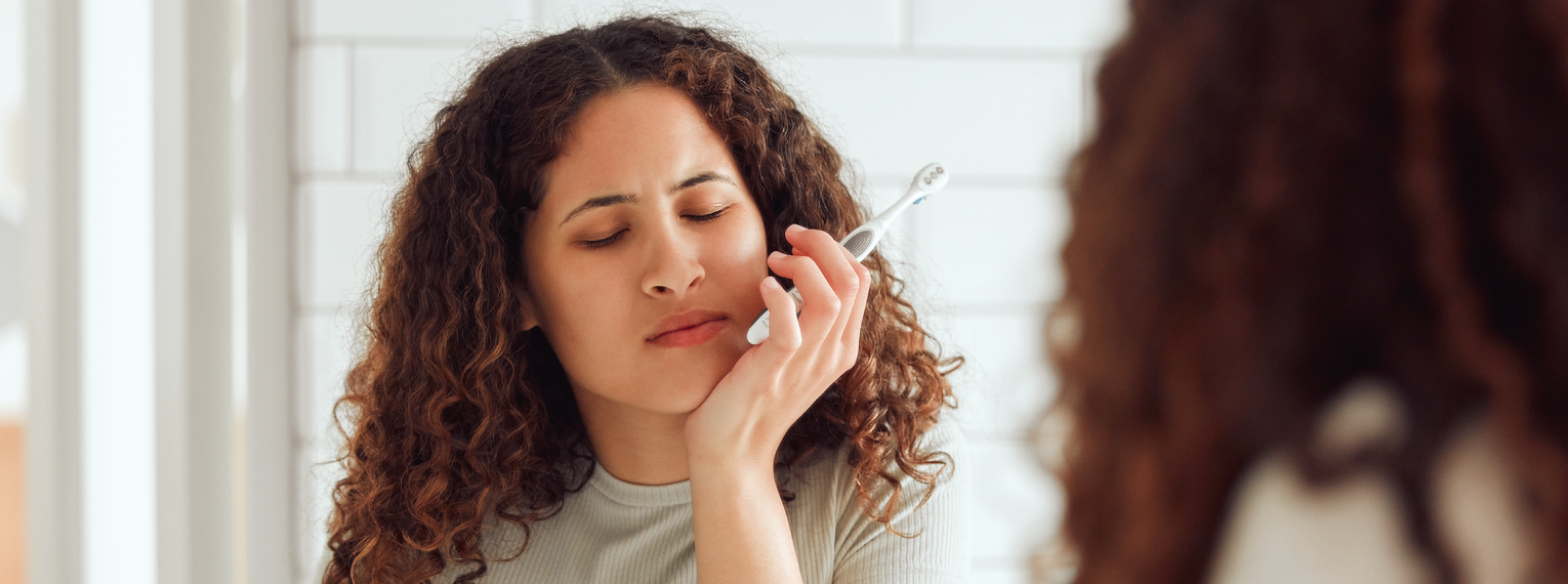 Eine Frau hält sich die Wange, weil sie Zahnschmerzen wegen einer Zahnfleischentzündung hat.
