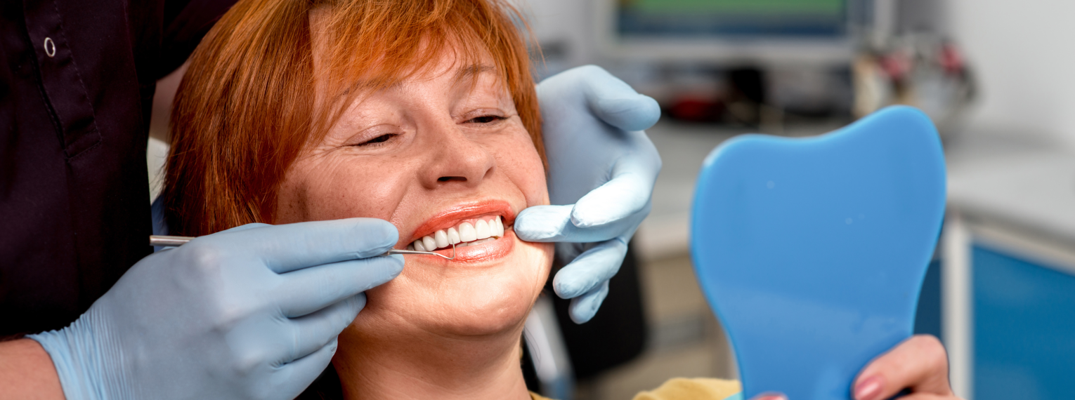 Eine Patientin mit Zahnfleischentzündung wird von einem Zahnarzt behandelt und lächelt dabei in einen Spiegel.