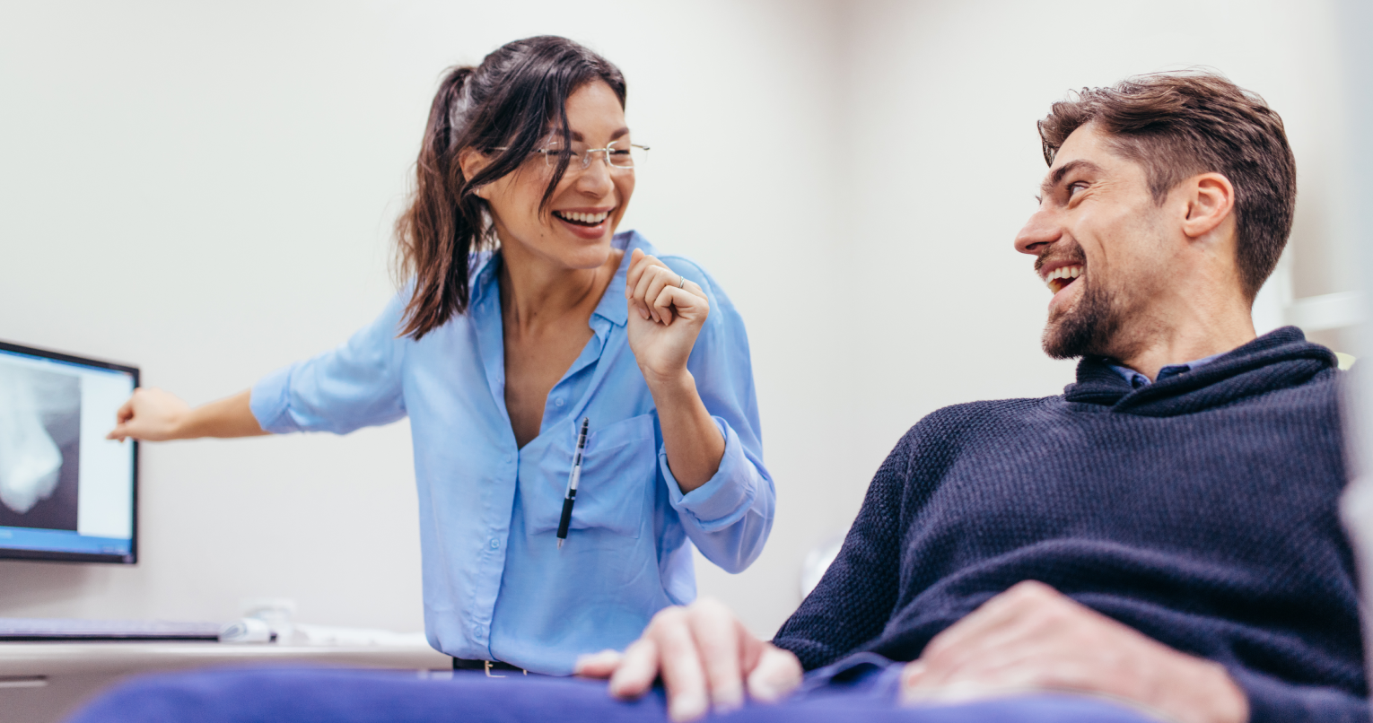 Eine Zahnärztin und ein Patient lachen sich gegenseitig an.