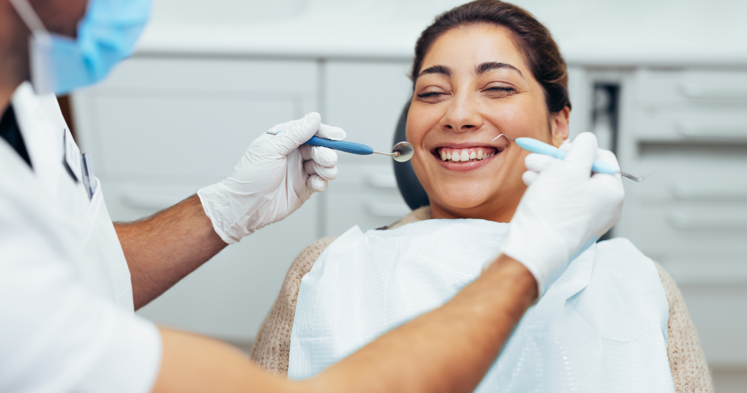 Eine lächelnde Patientin wird von einem Zahnarzt behandelt.