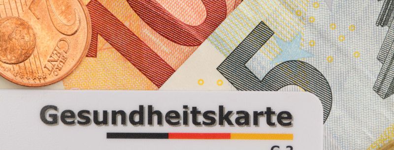 Zu sehen ist eine Krankenkassenkarte auf Geldscheinen, die zeigen sollen, wie hoch die Kostenübernahme der Krankenkasse ist.