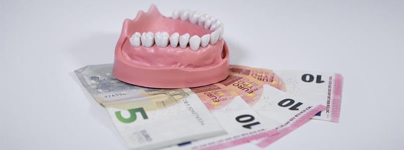 Zu sehen ist eine Zahnkrone auf Geldscheinen, um zu verdeutlichen, wie hoch die Zahnkrone Kosten ausfallen können.