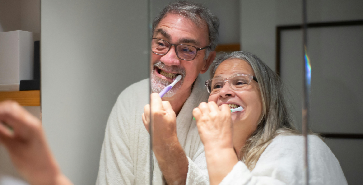 Ein Seniorenpaar schaut beim Zähneputzen in den Spiegel.